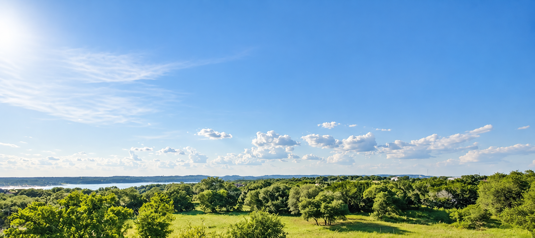 Treetops and Lake Travis beneath an open blue sky, viewed from a third-floor terrace in Canopy